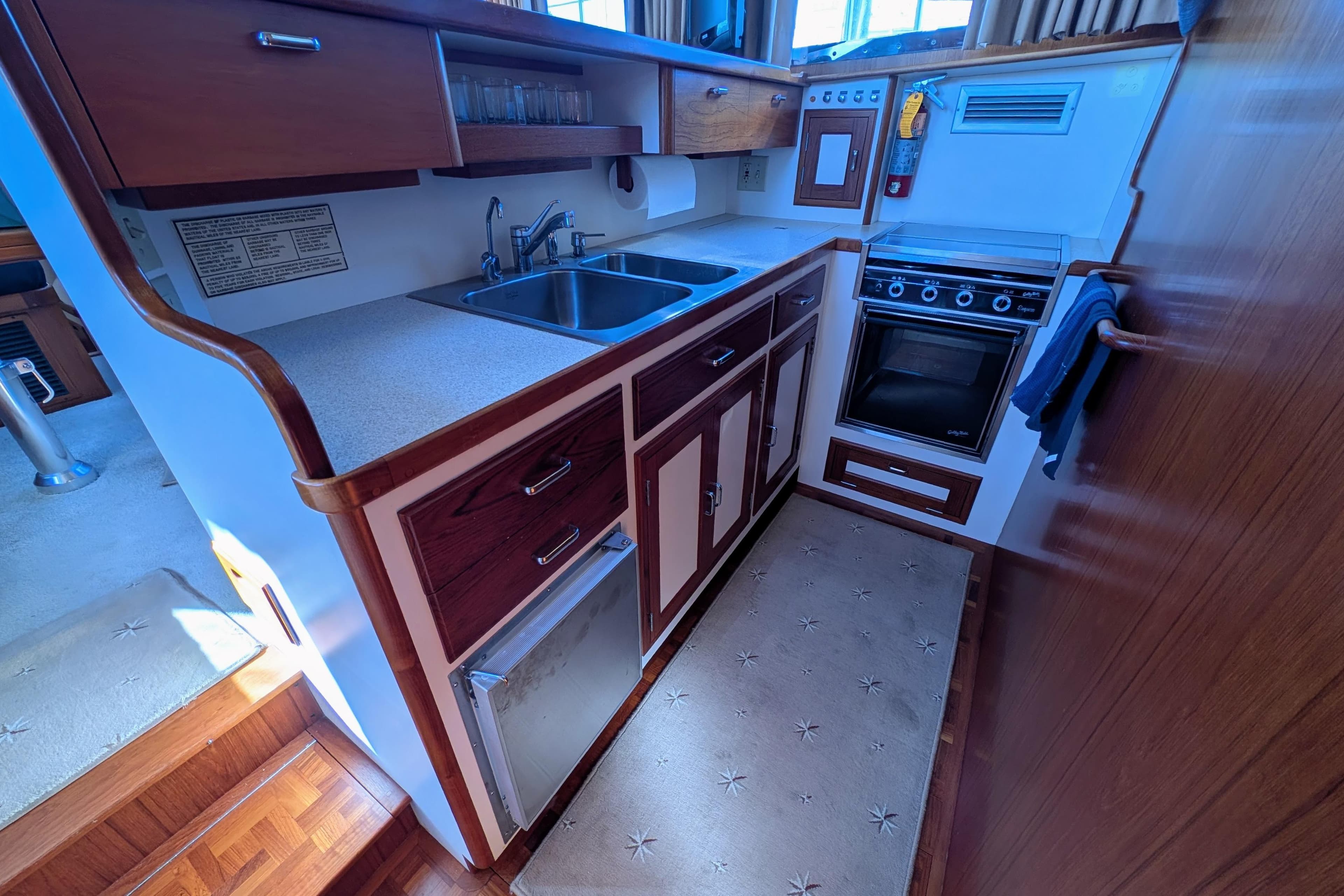Compact kitchen in a 2001 Dettling 51 yacht, featuring wood cabinetry and modern appliances.