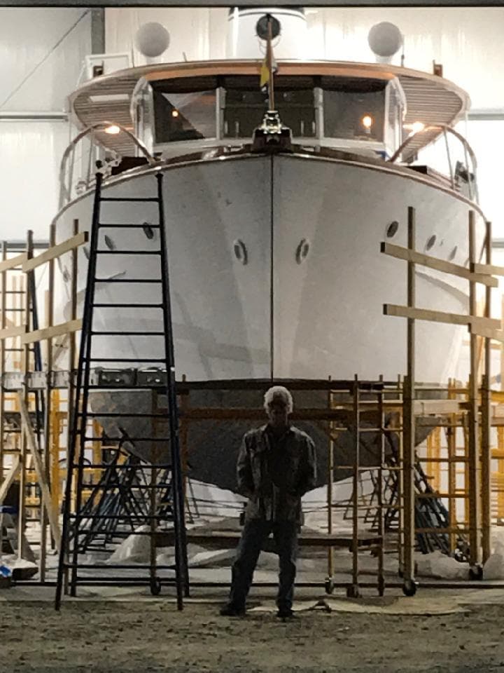 1947 Trumpy "60" Houseboat in a workshop with scaffolding and a person standing in front.
